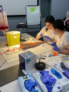 Students in a lab prepare to practice a medical procedure on a prosthetic leg. The leg is attached to an intravenous bag.