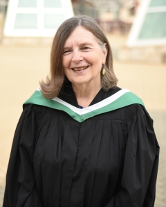 Woman in green, white and black academic regalia stands outside