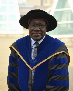 Man in royal blue, gold and black academic regalia stands outside