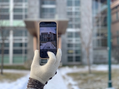 A hand shown holding a cell phone and taking a photo of a building