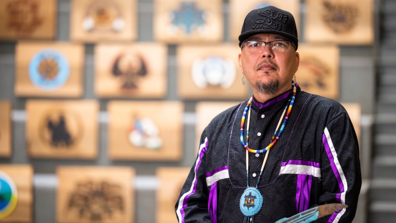 Artist Clayton Gauthier stands in the Canfor Winter Garden in front of 32 hand-carved cedar planks representing northern First Nations. 