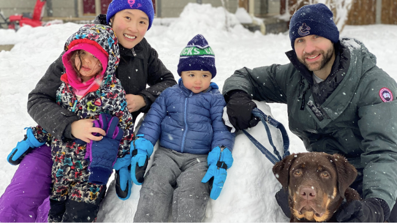 A mother and father with their two young children and dog outside in the snow.