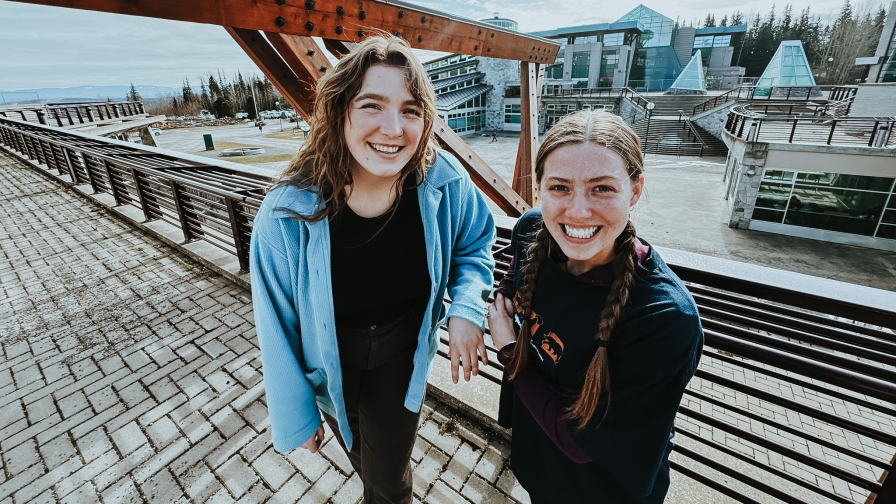 Two students outside at UNBC's Prince George campus with the Agora courtyard in the background 