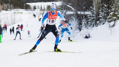 cross-country skiing athlete wearing white, light blue and navy blue race suit, skiing uphill