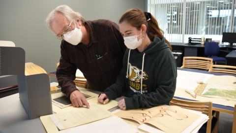Two people, wearing face masks, examine archival documents