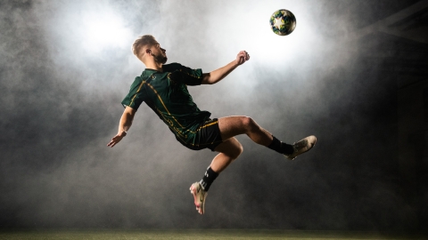 A soccer player wearing the new UNBC Indigenous uniforms preforms a bicycle kick with a smoke machine