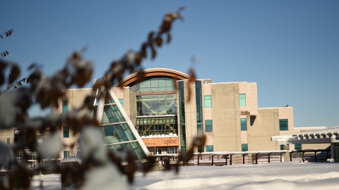 In the foreground snow covered branches, in the background, the UNBC library in winter