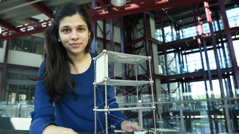 Civil Engineering Assistant Professor Dr. Ramla Qureshi in the Teaching an Learning Building posing next to a small metal building model with wood slabs. 