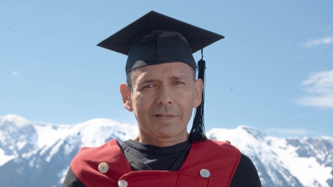Christopher Morven in regalia and academic cap with mountains in the background. 